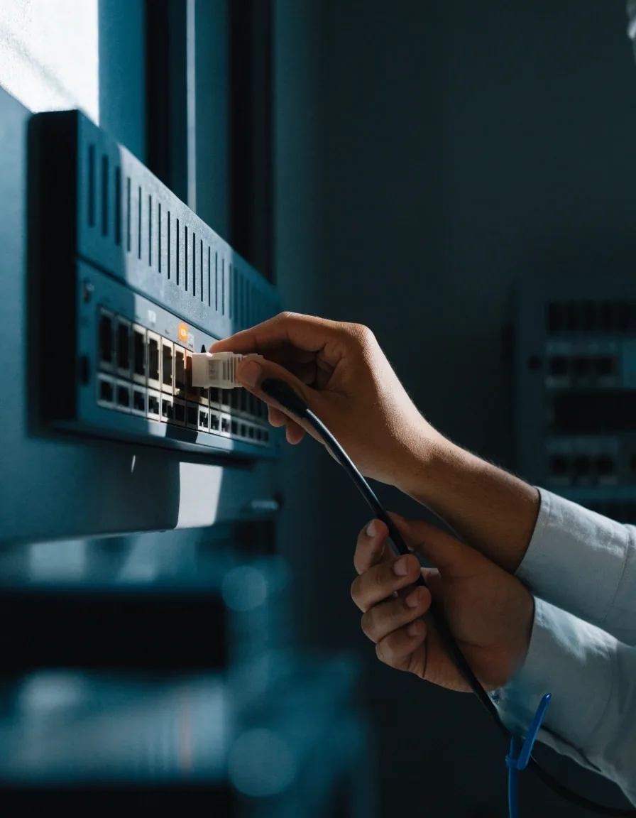 A technician's hand on a network rack in a dim server room, cabling dressed down the side